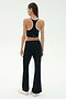 A woman faces away, wearing SPLITS59's Blaire Rib Pant in black with a black racerback crop top, styled with white sneakers against a plain light background.