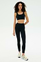 A woman wears the SPLITS59 Airweight Rib Bra in black, paired with black high-waisted leggings and white athletic shoes against a plain white background.