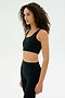 A woman with curly hair models the SPLITS59 Airweight Rib Bra in black, paired with matching leggings, standing against a plain white background and facing slightly to the side.
