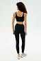 A woman with curly hair stands facing away against a plain light background, wearing the SPLITS59 Airweight Rib Bra in black and matching leggings crafted from stretchy nylon-spandex fabric.