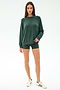 A woman stands against a plain background wearing the SPLITS59 Andie Fleece Sweatshirt in Military, matching green shorts, and white sneakers with green stripes.