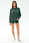 A woman stands against a plain background wearing the SPLITS59 Andie Fleece Sweatshirt in Military, matching green shorts, and white sneakers with green stripes.