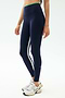 A person wears SPLITS59 Easton Rigor High Waist 7/8 leggings in Indigo/Grass—navy blue with side stripes, made from compressive fabric—with white sneakers, shown from shoulders down against a plain background.