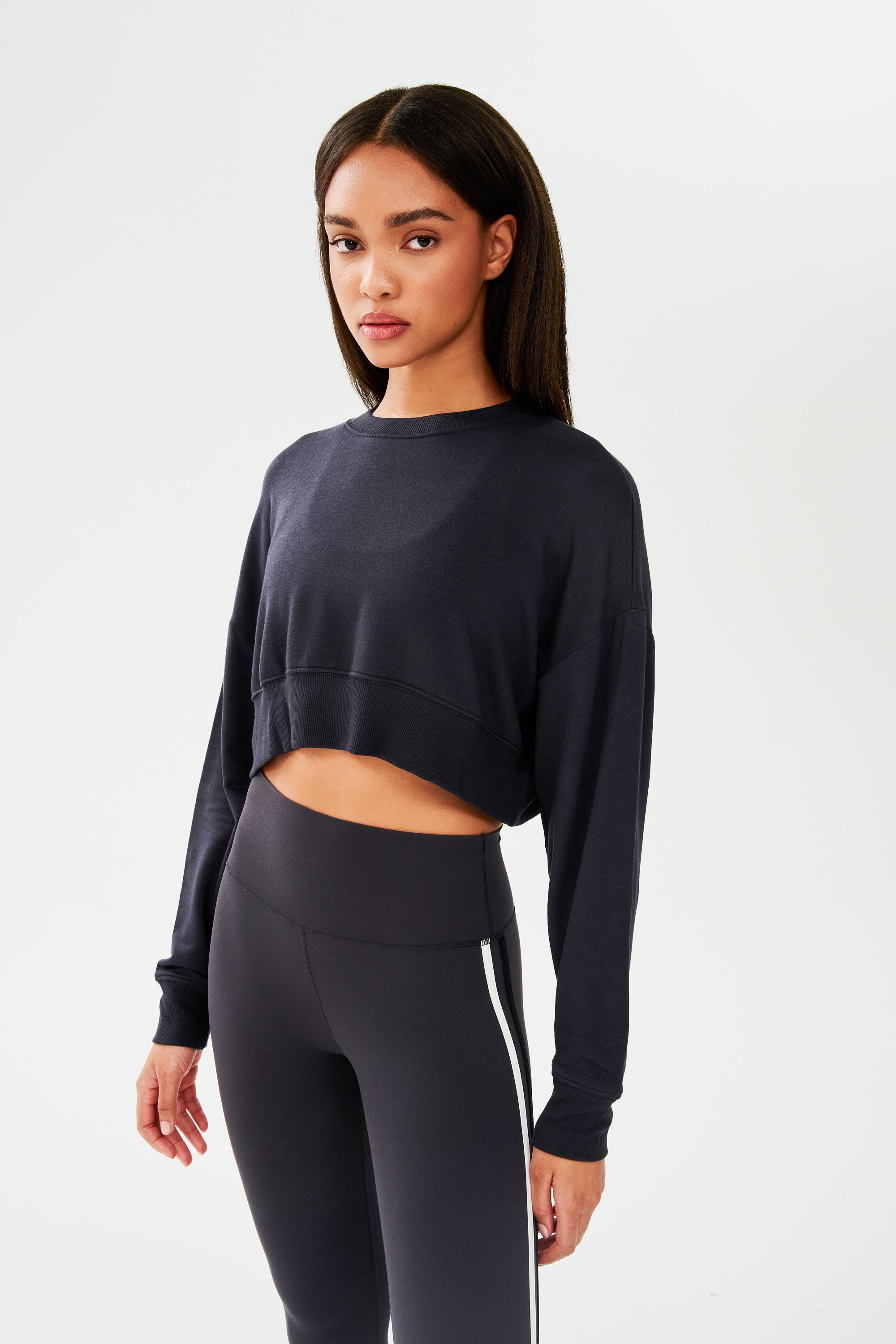 A woman wearing a SPLITS59 Noah Fleece Crop Sweatshirt in Graphite and athletic leggings.