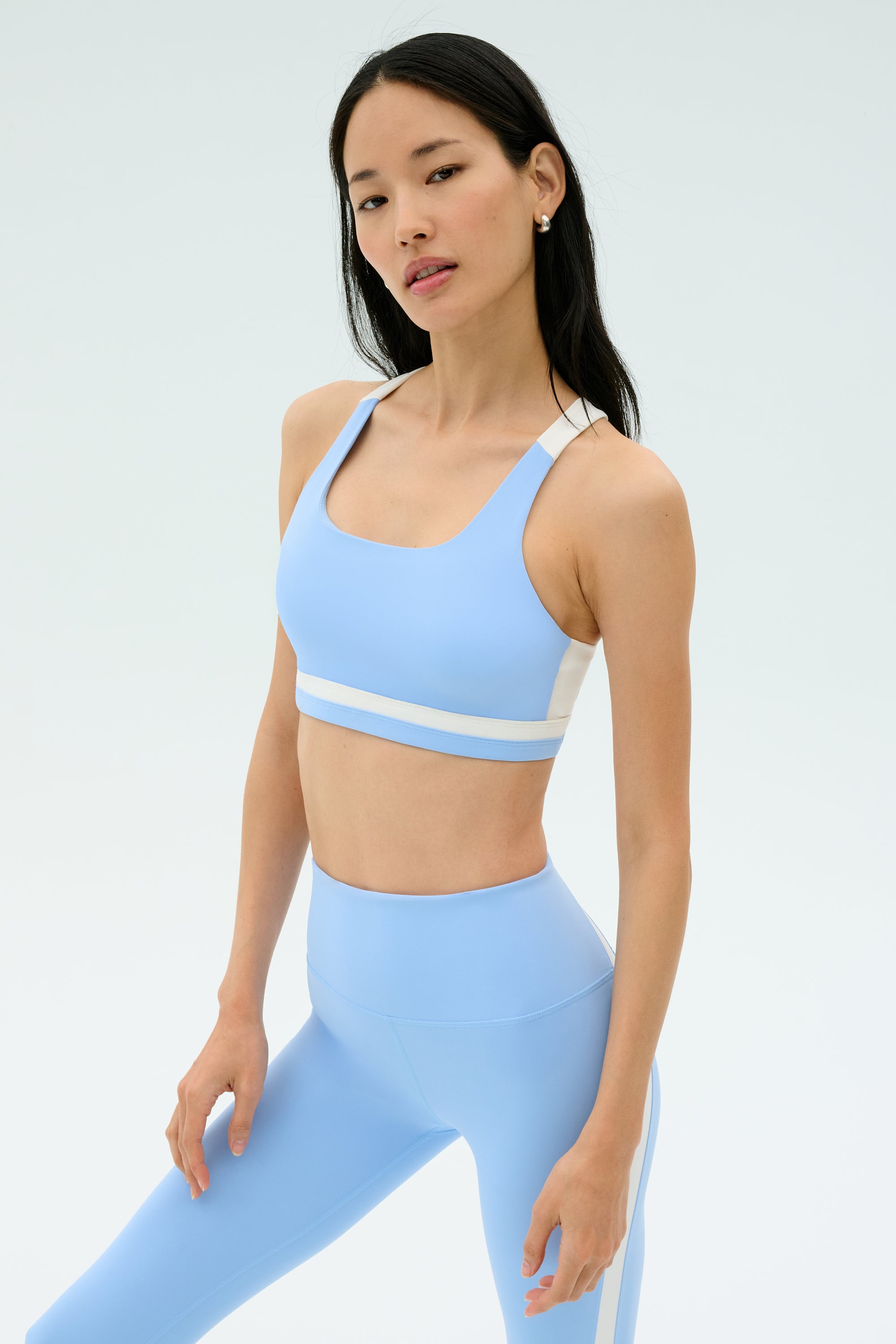 A woman stands against a plain background wearing the SPLITS59 Miles Rigor Bra in Skylight/White.