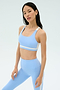 A woman stands against a plain background wearing the SPLITS59 Miles Rigor Bra in Skylight/White.