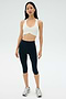 A woman stands facing forward against a plain light background, wearing the SPLITS59 Airweight Bra with Ruching in white, navy blue athletic leggings, and silver running shoes.