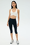 A woman stands facing forward against a plain light background, wearing the SPLITS59 Airweight Bra with Ruching in white, navy blue athletic leggings, and silver running shoes.