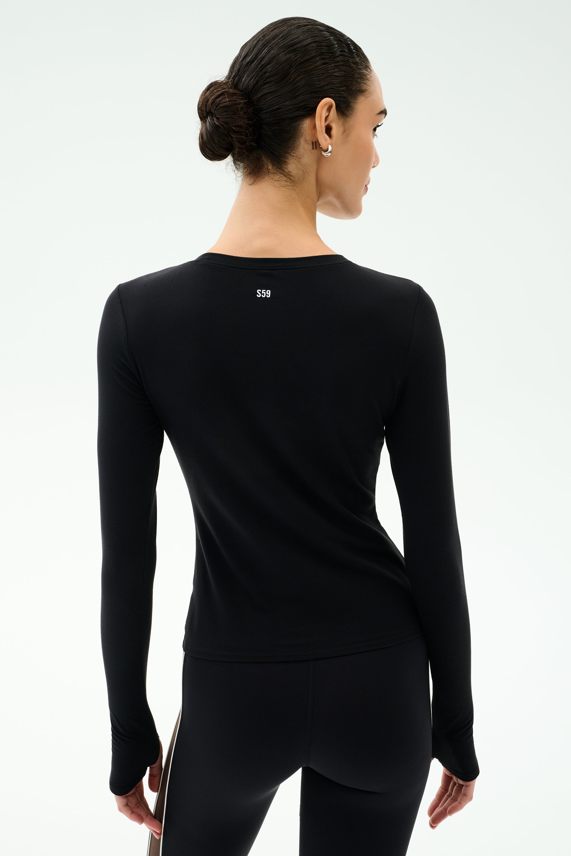 A person with dark hair in a bun wears the SPLITS59 Airweight Lite Long Sleeve Waist Length tee in black, paired with black leggings, shown from the back against a plain light background—ideal for quick-dry comfort during workouts.