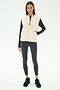A woman wears the SPLITS59 Aster Sherpa Vest - Creme, a cozy layer for cool weather workouts, over a black long-sleeve top, leggings, and sneakers, standing against a plain white background.