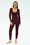 A person stands barefoot against a white background, wearing the SPLITS59 Chloe Airweight Jumpsuit in Dark Cherry—a fitted, long-sleeve piece with a scoop neckline made from smooth nylon spandex.