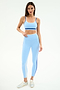 A woman poses against a plain background wearing the SPLITS59 Eva Rigor Double Strap Bra in Skylight/Cobalt, paired with matching leggings and silver sneakers.