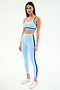 A woman stands against a plain white background wearing the SPLITS59 Eva Rigor Double Strap Bra in Skylight/Cobalt and matching high-waisted leggings with dark blue stripes, paired with white sneakers.