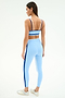 A woman faces away in a light studio wearing SPLITS59’s Eva Rigor Double Strap Bra in Skylight/Cobalt, paired with high-waisted vertical stripe leggings.