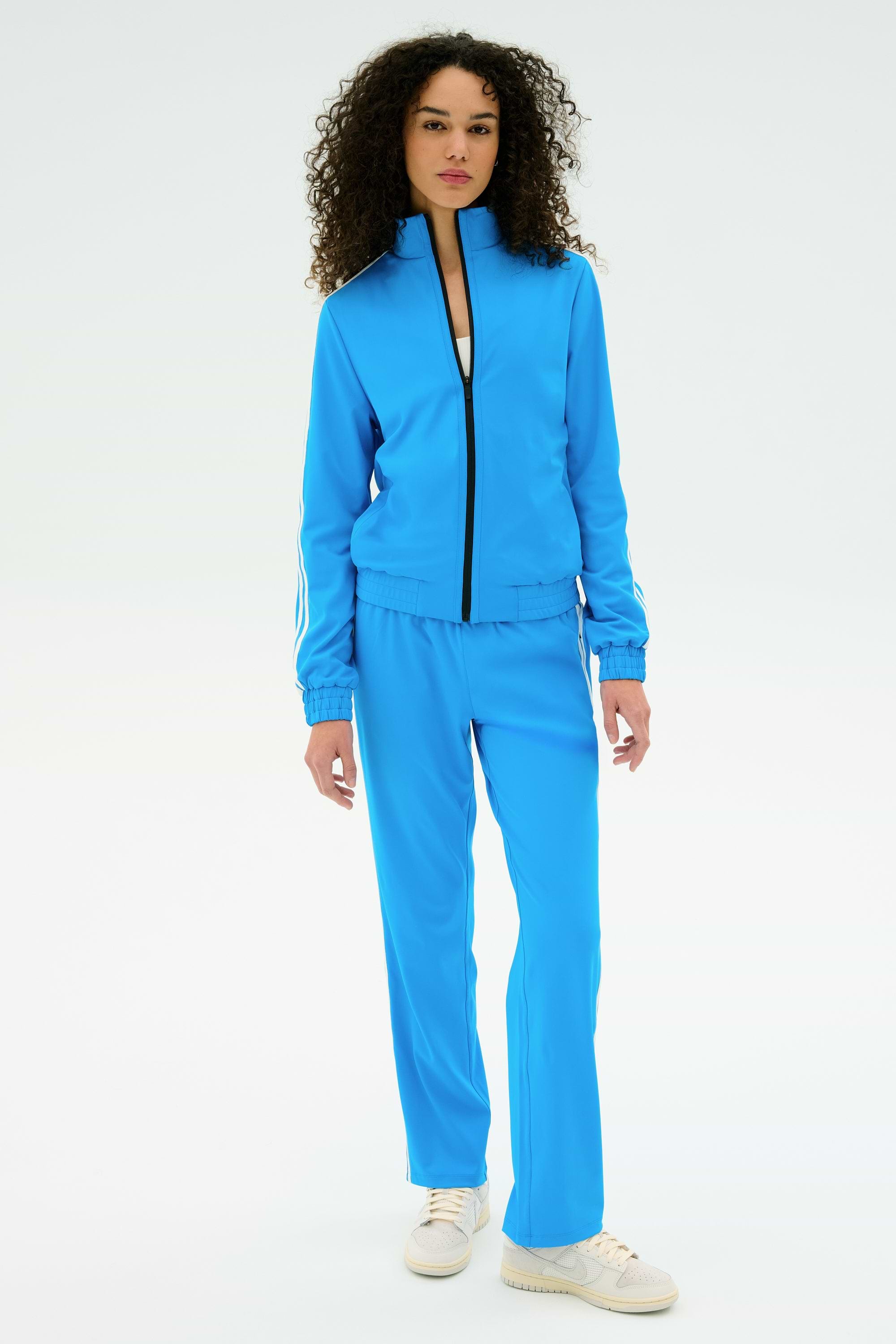 A person stands facing forward in the SPLITS59 Fox Techflex Jacket in Riviera/White and white sneakers, set against a plain white background.