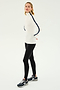 A person wearing a SPLITS59 Jackson Rib Full Length Turtleneck in White/Indigo with black stripes on the sleeves, paired with black leggings and black athletic shoes, stands against a plain white background—ready for a yoga or Pilates session.