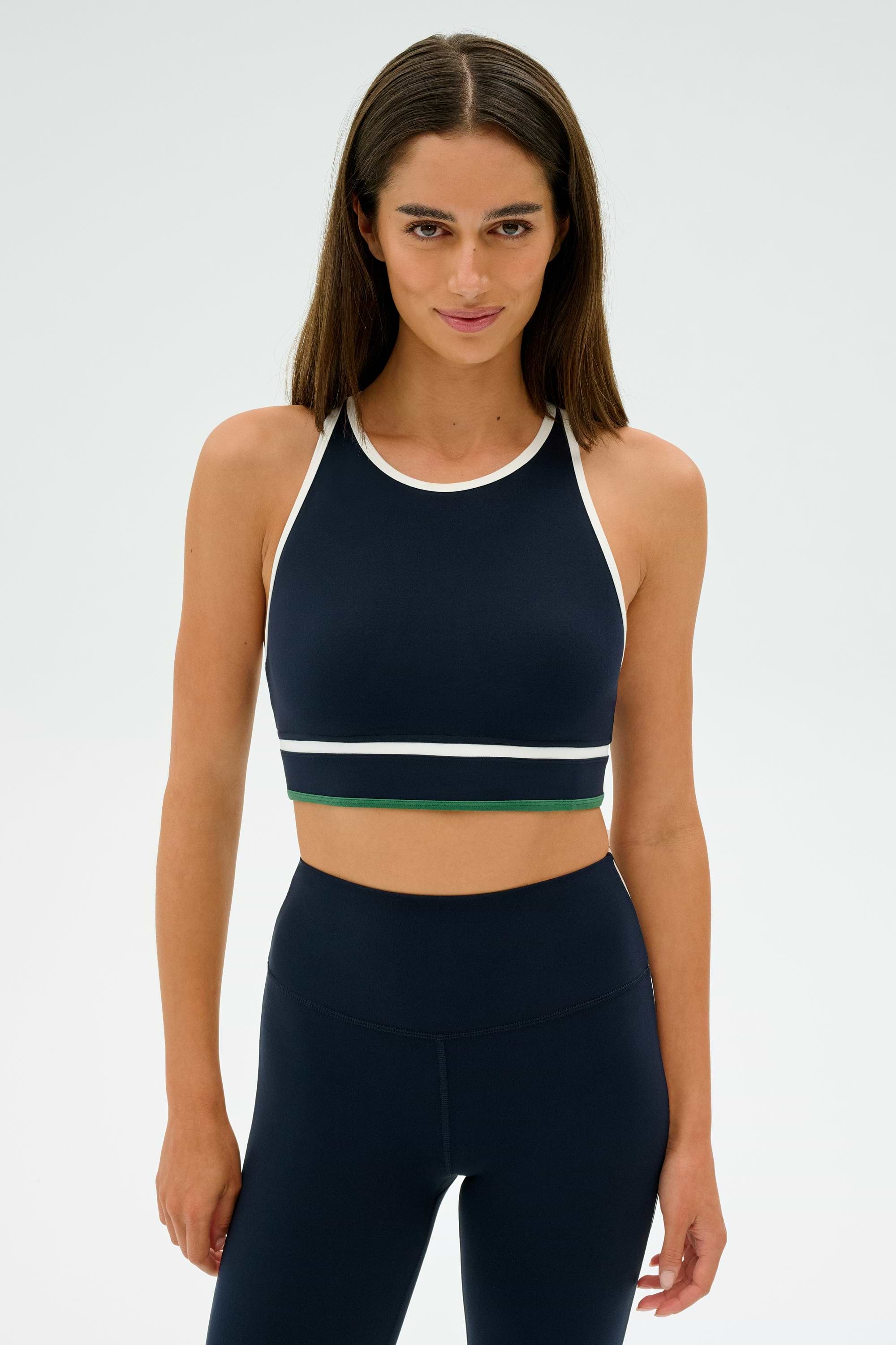 A person is standing against a plain background, wearing the Layla Airweight Bra in Indigo/White by SPLITS59, paired with navy blue leggings.