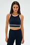 A person is standing against a plain background, wearing the Layla Airweight Bra in Indigo/White by SPLITS59, paired with navy blue leggings.