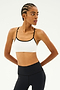 Against a white backdrop, an individual wears the Loren Seamless Bra in White/Black by SPLITS59, paired with black leggings. Their arms are positioned behind their back, showcasing a readiness for gym workouts while enjoying chafe-free comfort.