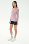 A woman stands against a plain white background wearing the SPLITS59 Louise Rib Henley in Blush, navy bike shorts, white sneakers, and white crew socks.
