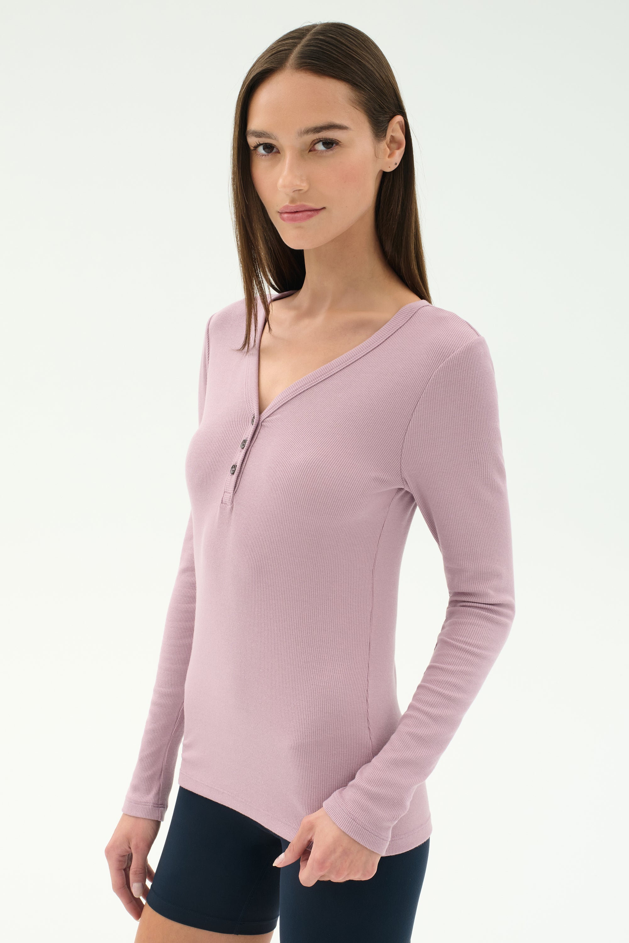 A woman with straight brown hair wears the SPLITS59 Louise Rib Henley in blush and black shorts, standing against a plain white background.