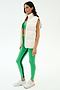 A woman stands in profile against a plain background wearing the SPLITS59 Summit Nylon Puffer Vest in white, paired with a green sports bra, green leggings with black stripes, and white athletic shoes—ideal for cool weather workouts.