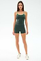 A woman faces forward against a plain light background, wearing SPLITS59’s Airweight High Waist 3.5” Short in Military with a matching dark green tank top and white sneakers. The outfit is made from a stretchy nylon-spandex blend.