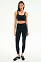 A woman faces forward in a SPLITS59 Airweight Rib Bra - Black and matching high-waisted leggings, crafted with moisture-wicking fabric for hot yoga, paired with black sneakers against a plain white background.