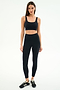 A woman faces forward in a SPLITS59 Airweight Rib Bra - Black and matching high-waisted leggings, crafted with moisture-wicking fabric for hot yoga, paired with black sneakers against a plain white background.