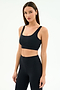 A woman with straight brown hair wears the SPLITS59 Airweight Rib Bra in black, paired with high-waisted leggings, both made from moisture-wicking fabric, standing against a plain white background.
