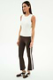 A woman stands against a plain white background wearing the SPLITS59 Carter Airweight Lite Tank in white, brown flared pants with a spandex side stripe, and brown Nike sneakers.