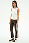 A woman stands against a plain white background wearing the SPLITS59 Carter Airweight Lite Tank in white, brown flared pants with a spandex side stripe, and brown Nike sneakers.