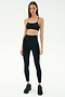 A woman stands against a plain white background wearing the SPLITS59 Airweight Super High Waist 7/8 leggings in black, paired with a black sports bra and athletic shoes—ideal for hot yoga sessions.