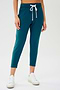 Front view of woman wearing a green and blue tone sweatpant with tapered leg and above ankle length with white drawstring and side hip pockets. Paired with white shoes.