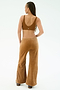 A person with long braids stands facing away, wearing the SPLITS59 Joy Velour Pant in Honey—a pair of tan wide-leg pants made from soft polyester spandex—paired with a brown sports bra against a plain light background.