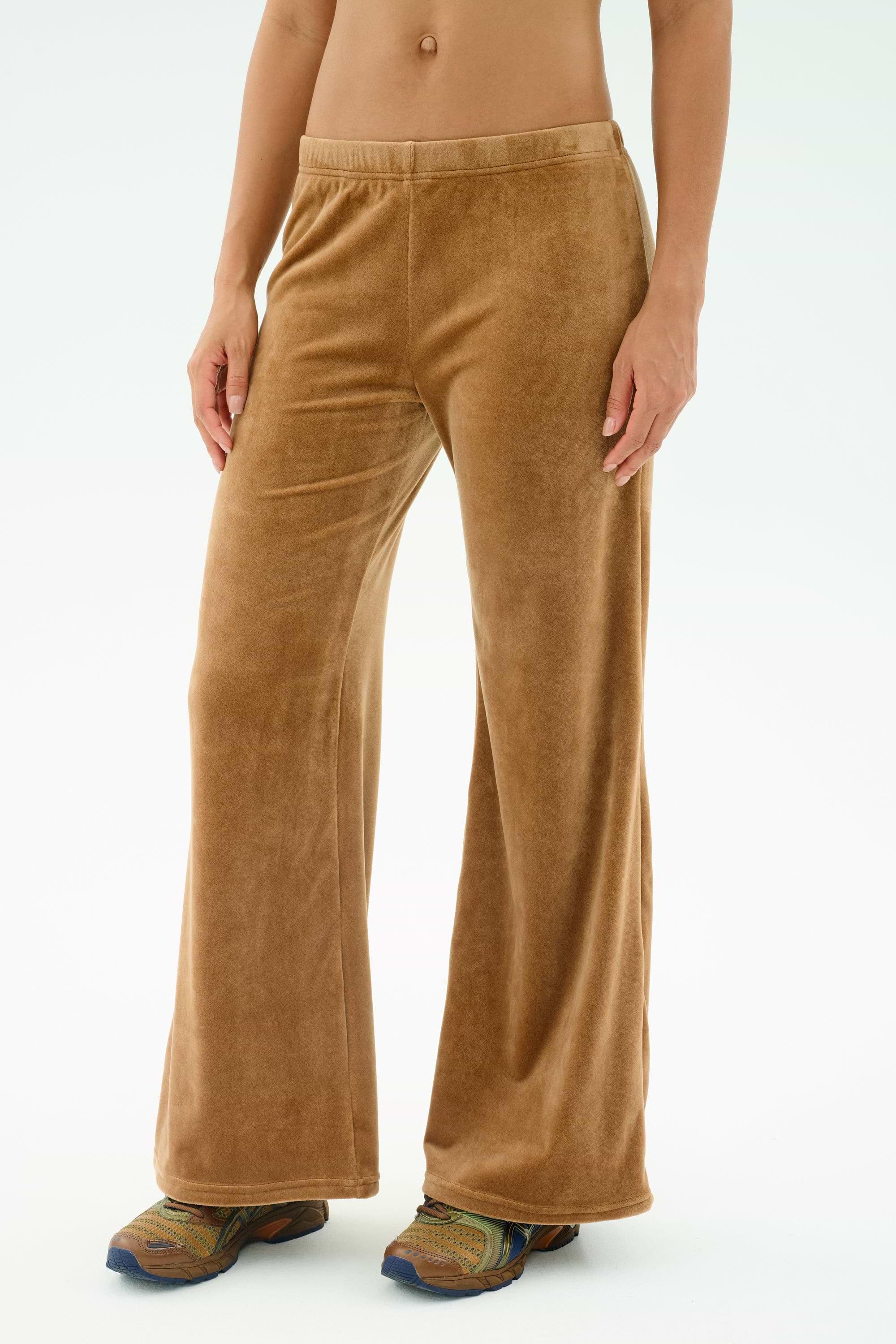 A person wearing SPLITS59's Joy Velour Pant in Honey, made from polyester spandex, paired with multicolored sneakers, is shown from midriff to feet against a plain background.