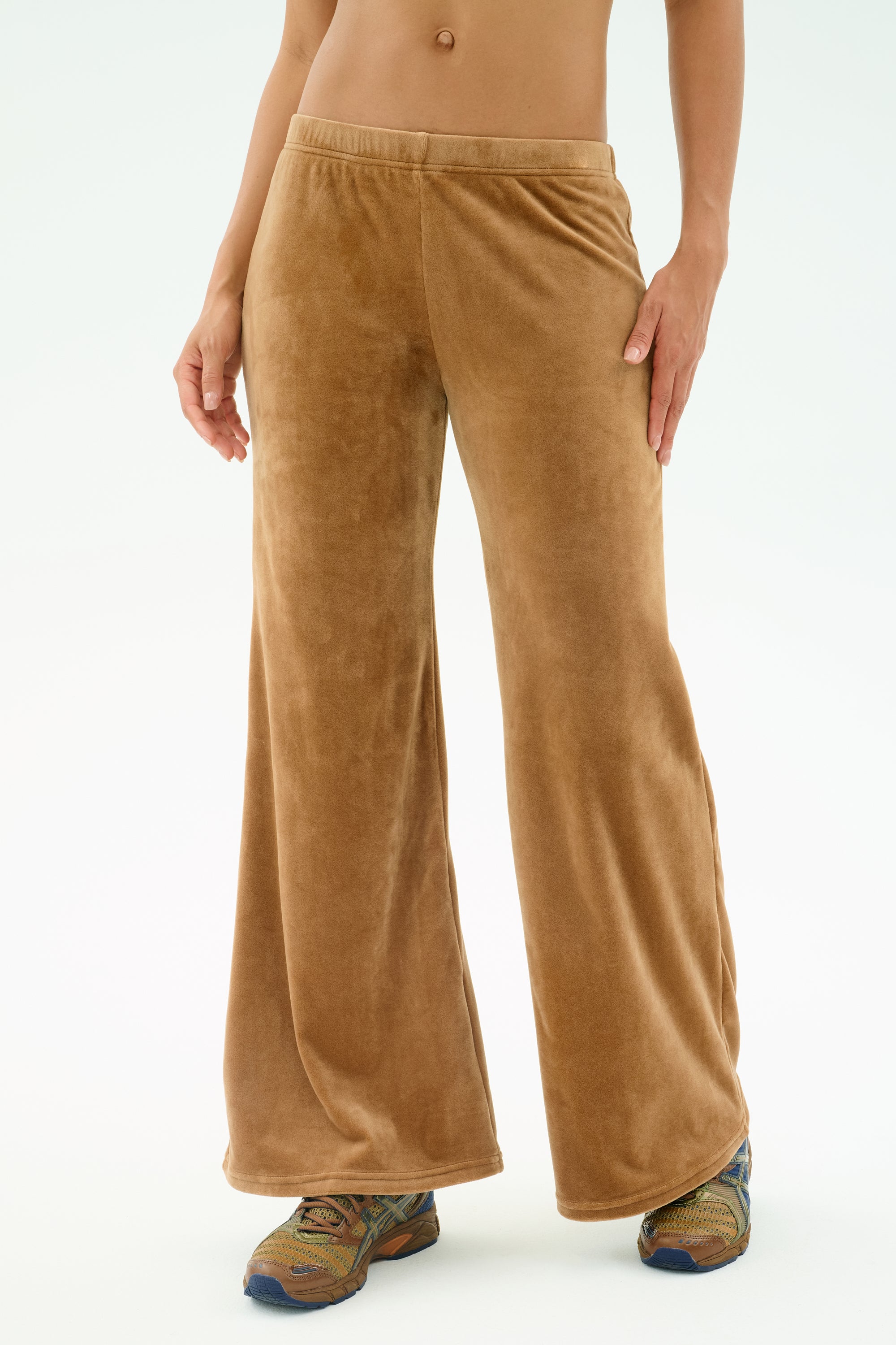 Someone wearing SPLITS59's Joy Velour Pant in Honey, featuring tan wide-leg design in polyester-spandex, and colorful sneakers, with a partially visible torso against a plain light background.