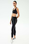 A person stands against a plain background wearing a black sports bra, SPLITS59 Margot Rigor Legging - Black/Dark Chocolate high-waisted leggings with side stripes, and white sneakers.