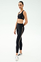 A person stands against a plain background wearing a black sports bra, SPLITS59 Margot Rigor Legging - Black/Dark Chocolate high-waisted leggings with side stripes, and white sneakers.