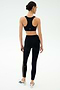 A woman faces away wearing a black sports bra, SPLITS59 Margot Rigor Legging in Black/Dark Chocolate, and white athletic shoes against a plain light background.