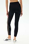 A person wears SPLITS59 Margot Rigor Legging in Black/Dark Chocolate, featuring a high waist, sheer side panel, and white stripe, paired with white sneakers against a plain background.
