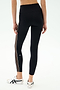 A person wears SPLITS59 Margot Rigor Legging in Black/Dark Chocolate, featuring a high waist, sheer side panel, and white stripe, paired with white sneakers against a plain background.