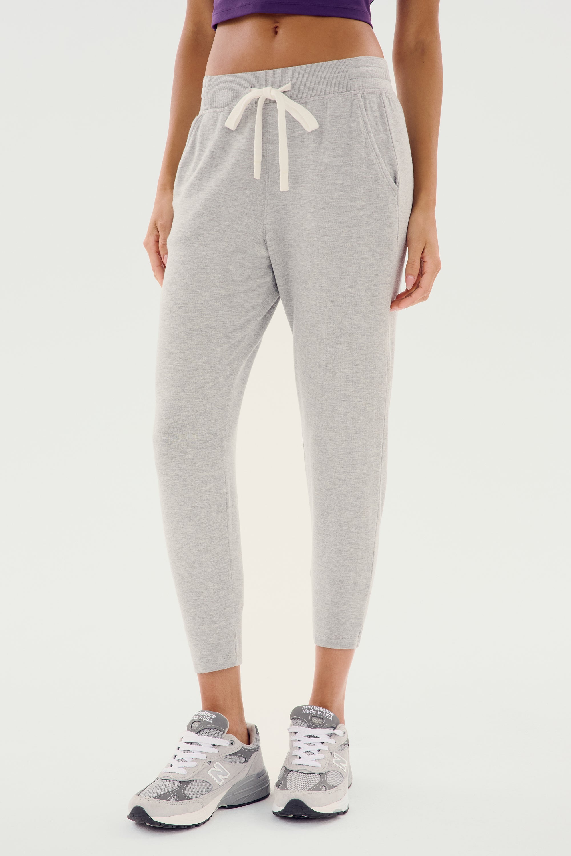 A person wearing the Splits59 Reena Fleece 7/8 Sweatpant in Heather Grey and matching gray sneakers stands against a white background, highlighting the front view of these everyday wear sweatpants with a drawstring waistband.
