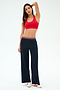 A woman stands against a plain background wearing a red sports bra, SPLITS59 Michele Airweight Trouser in Indigo with a striped waistband, and white sneakers with red stripes.