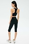 A woman faces away, wearing the SPLITS59 Airweight Bra with Ruching in Black, paired with black capri leggings and silver sneakers against a plain light background.