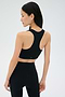 A woman in black athletic wear stands facing away, highlighting the back of the SPLITS59 Airweight Bra with Ruching and matching leggings, both crafted from ultra-light Airweight performance fabric, against a plain light background.