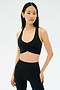 A woman stands against a plain background, wearing the SPLITS59 Airweight Bra with Ruching in black and high-waisted leggings, looking at the camera with a neutral expression.