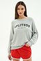 A woman stands against a plain white background wearing the SPLITS59 Andie Oversized Fleece Varsity Graphic Sweatshirt in Heather Grey/Splits59 Los Angeles and red athletic shorts.