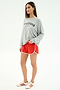 A woman wears the SPLITS59 Andie Oversized Fleece Varsity Graphic Sweatshirt in Heather Grey and red athletic shorts, styled with white sneakers. This cozy Los Angeles-made look features comfort and varsity flair.