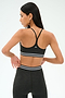 Woman with long dark hair and earrings stands against a plain background, seen from the back, wearing the SPLITS59 Cali Active Rib Bra in Heather Graphite. The sports bra features white stripes and offers supportive comfort.